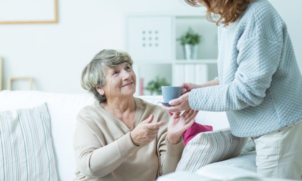 a girl is giving a cup of tea to an old woman